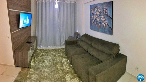 Sala de estar com sofá retrátil, smart tv e varanda. 