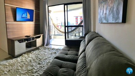 Sala de estar com sofá retrátil, smart tv e varanda. 