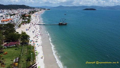 Praia de Canasvieiras e trapiche de Canasvieiras com barco de passeio atracado e ilha do Francês ao fundo