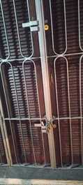 Porta da casa com 3 cadeados e grade, janelas com grade