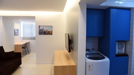 à direita: maquina lavar e gelágua; à esquerda, sala com sofa-cama e tv; e, ao fundo, bancada de tr