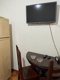 Sala: geladeira duplex, mesa com 3 cadeiras, tv no suporte, sofá-cama e  1 ventilador de teto 