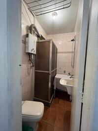 Banheiro: vaso sanitário, secador de roupa de teto, aquecedor a gás, box com chuveiro, mesa, armário de banheiro e pia tanque 
