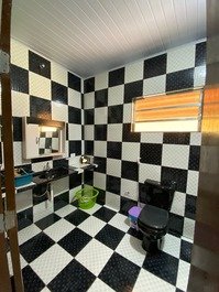 Banheiro da suíte com chuveiro elétrico, apetrechos para cabelo, espelho 