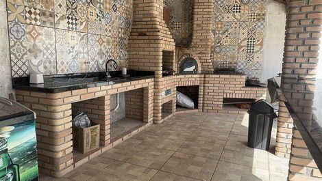 Área da churrasqueira com pia, forno a lenha e fogão a lenha com freezer horizontal