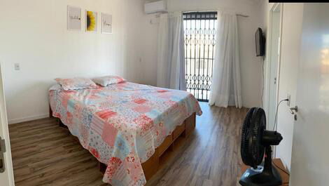 Quarto com cama queen e gavetas, ar condicionado ventilador de chão e banheiro completo com secador de cabelos.